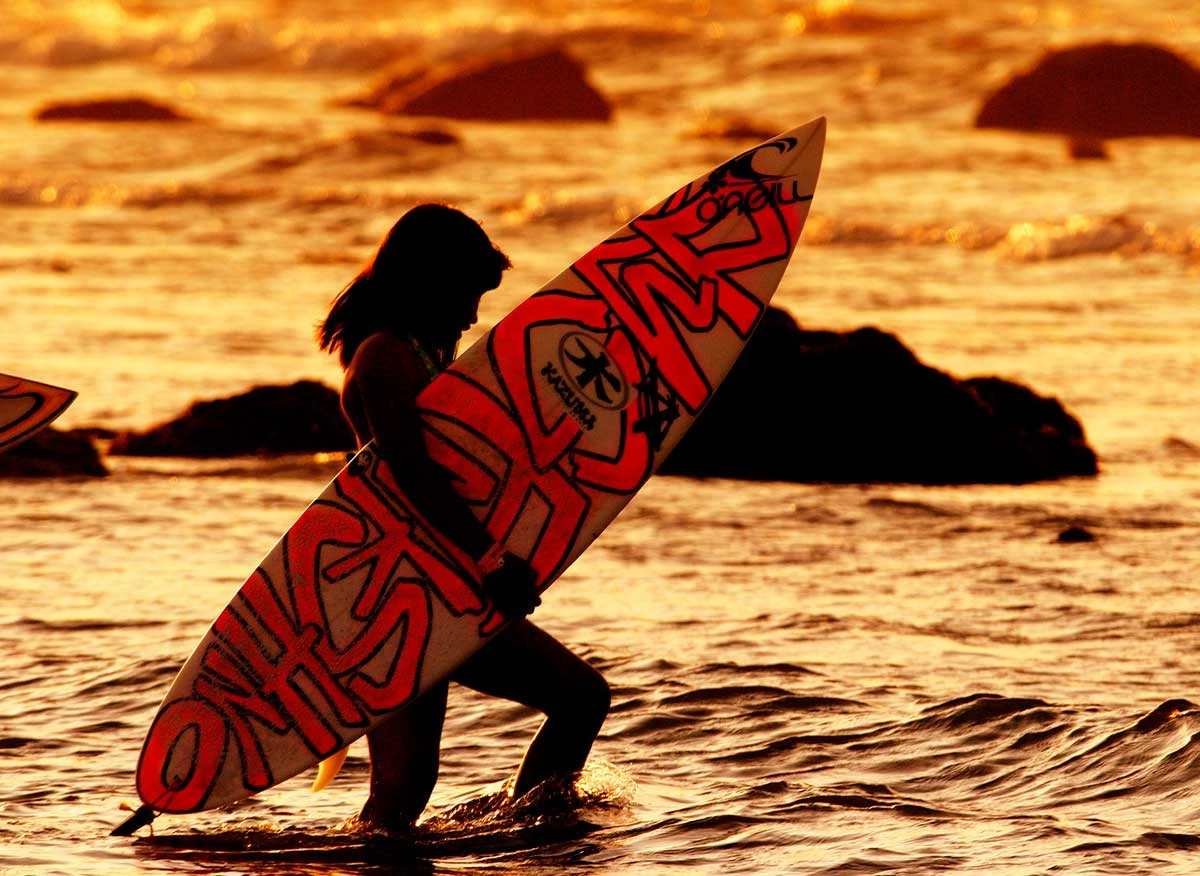 Surfista entrando al mar al atardecer en Máncora