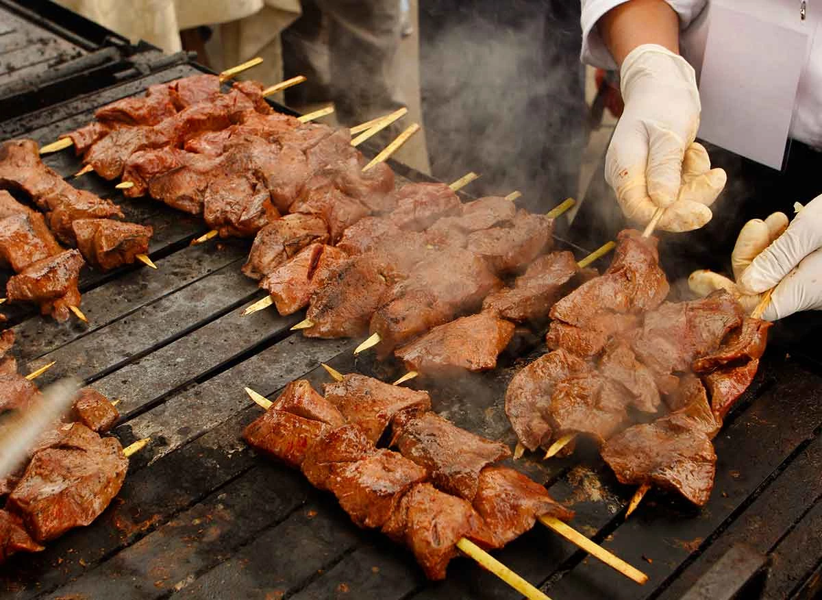 Anticuchos de corazón de res dorándose sobre la parrilla